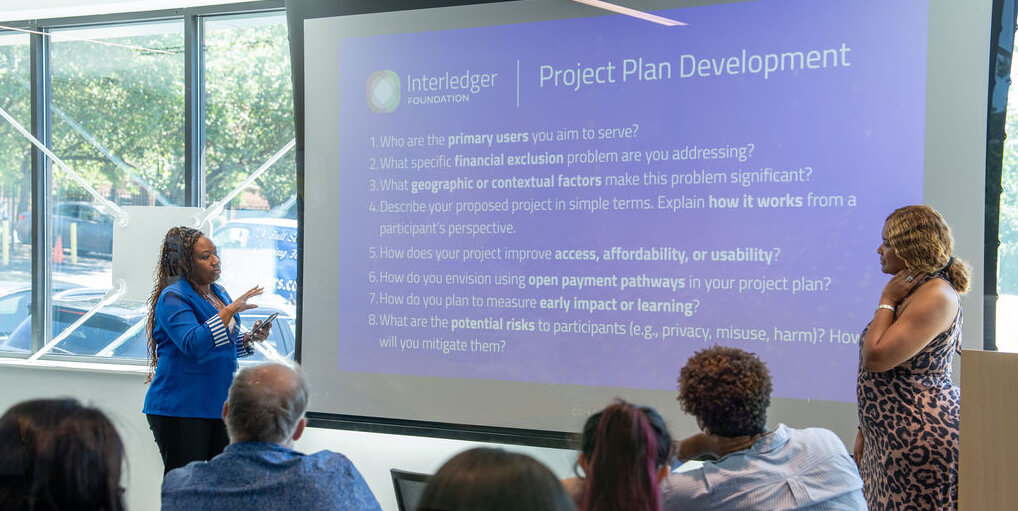Two presenters speaking in front of a slide titled āProject Plan Development,ā sharing ideas and strategies